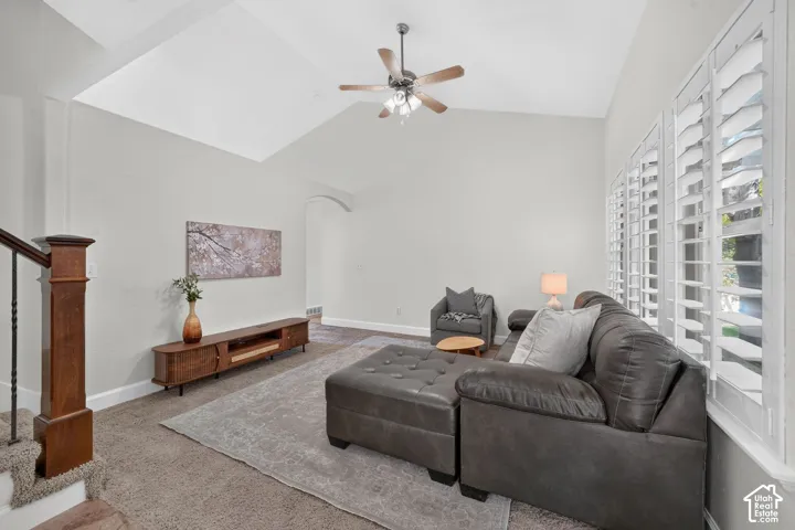 Vaulted ceiling with a ceiling fan, white plantation shutters, dark wood-finish newel post with wrought iron spindles, and a light gray wall finish