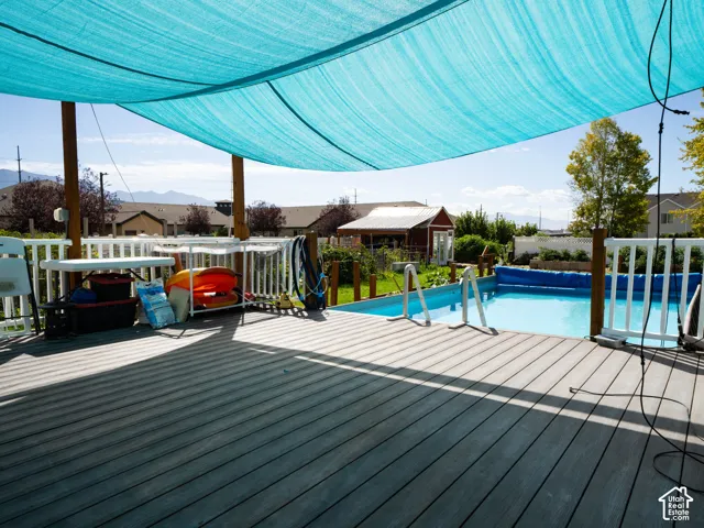 Expansive wood-finish deck with a turquoise shade canopy, overlooking an in-ground swimming pool