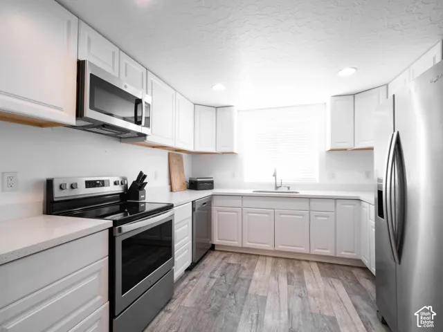 White cabinetry, stainless steel appliances, wood-finish flooring, white countertops, and recessed lighting
