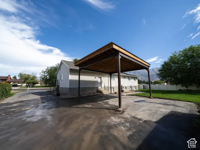 Detached carport structure, side-gabled residence with light-colored siding, paved driveway, and established lawn area
