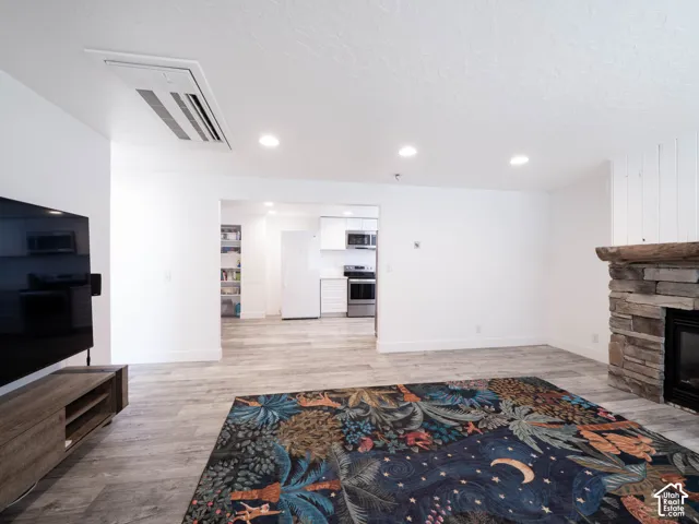 Stone-clad fireplace with a wood mantle, wood-finish flooring, and recessed ceiling lighting