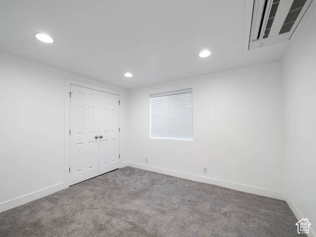 Recessed ceiling lighting, white walls, gray carpet flooring, white window blinds, and white bi-fold closet doors