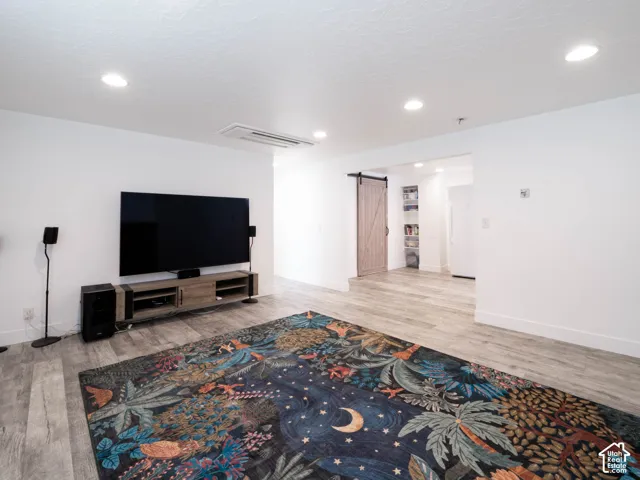 Recessed lighting, wood-finish flooring, white walls, and a barn-style door