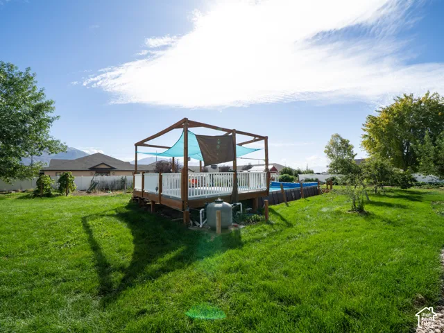 Expansive green lawn with a wooden deck featuring a pergola structure and a visible pool