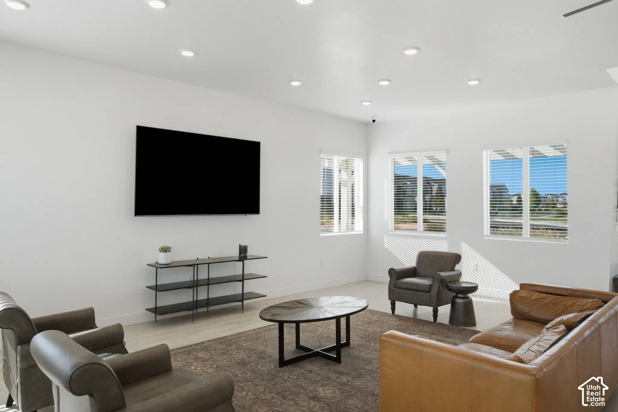Recessed lighting throughout, multiple windows with blinds, wood-finish flooring, and a wall-mounted entertainment display