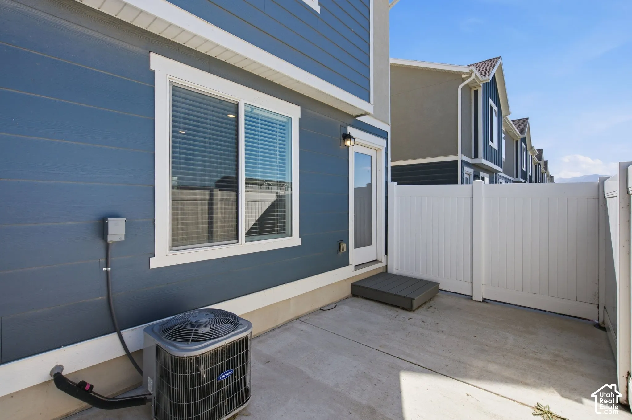 Private fenced patio with a concrete surface, featuring a rear entry door and a white vinyl fence