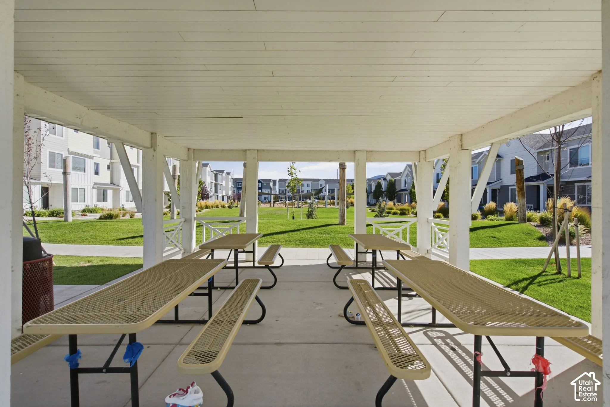 Covered outdoor dining area with multiple picnic tables, concrete flooring, and surrounding green space