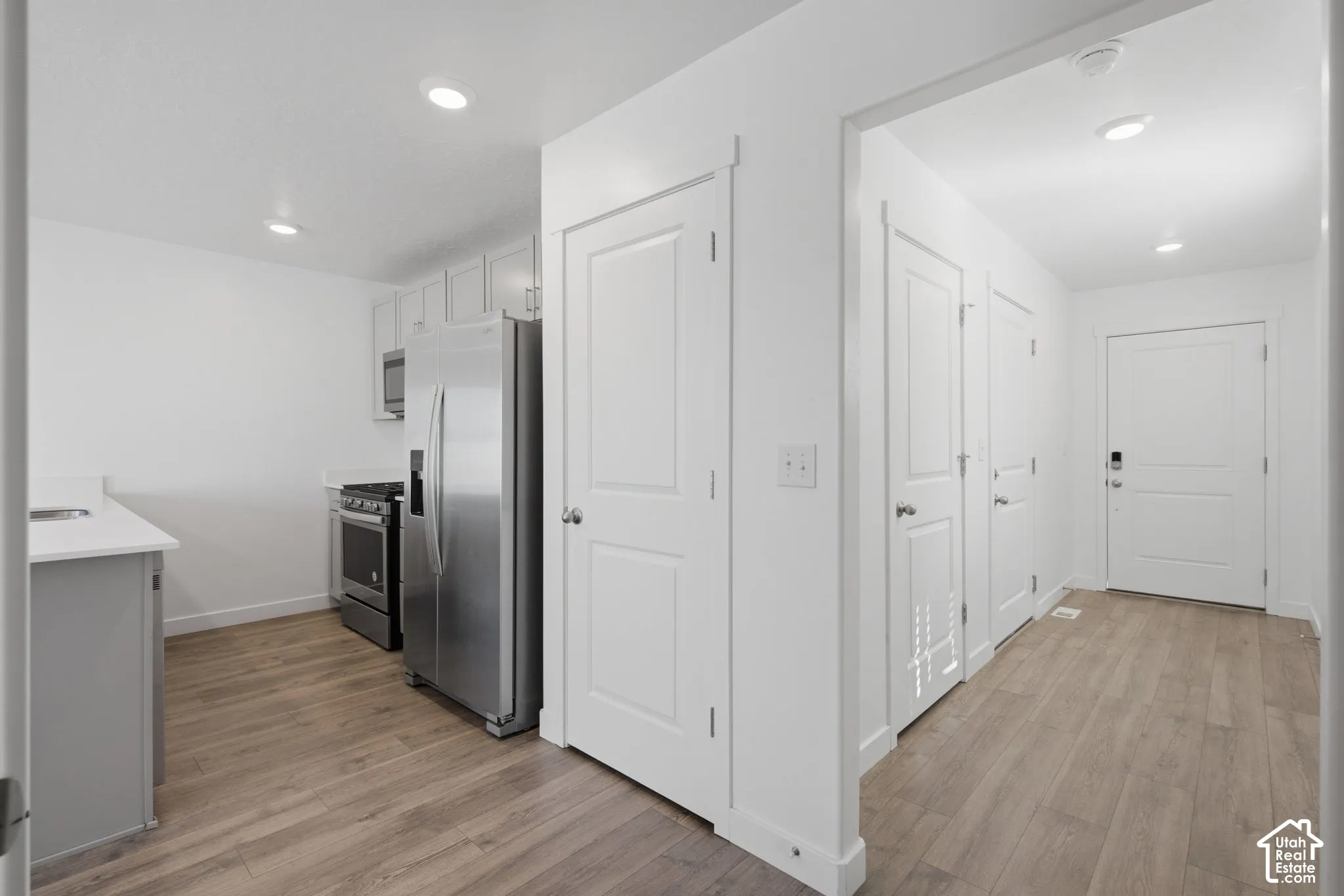 Kitchen featuring stainless steel appliances, light-toned cabinetry, light countertops, and wood-finish flooring