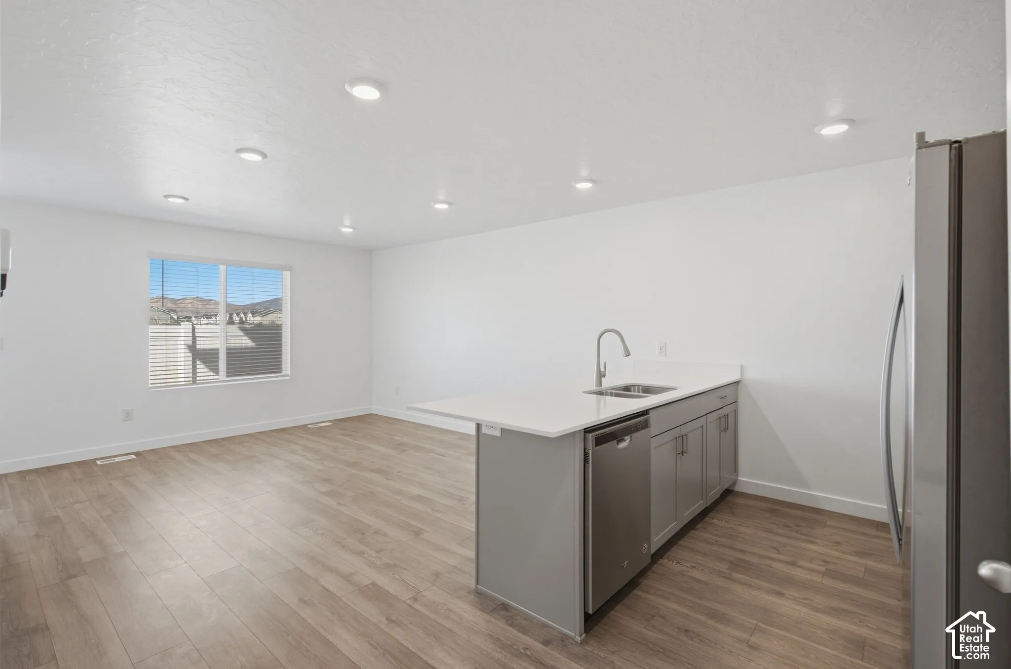 Open-concept living area featuring wood-finish flooring, recessed lighting, a kitchen island with an undermount sink and stainless-steel appliances, and a window with mountain scenery