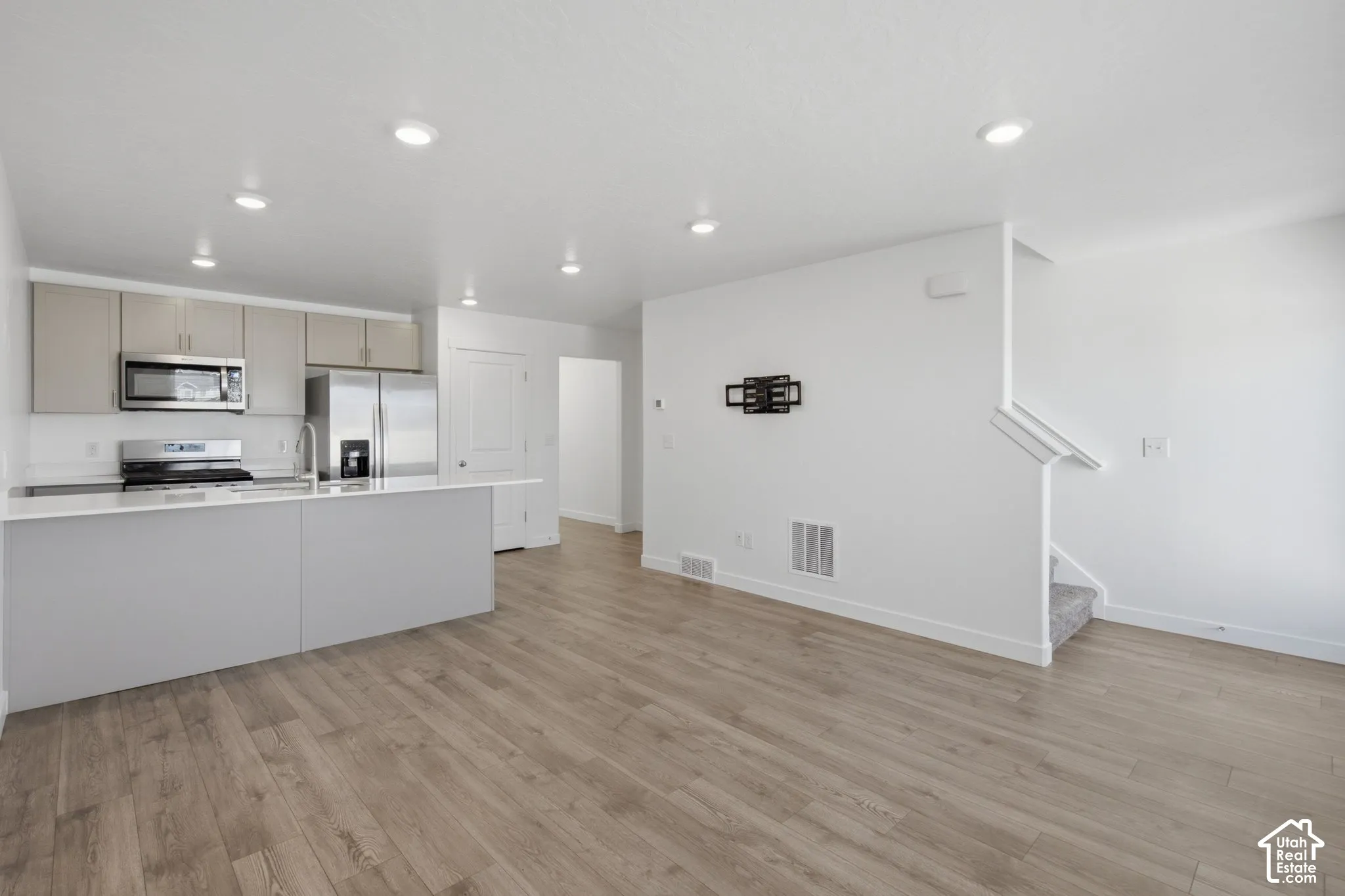 Kitchen with stainless steel appliances, light wood-finish flooring, recessed lighting, and a kitchen island with a sink
