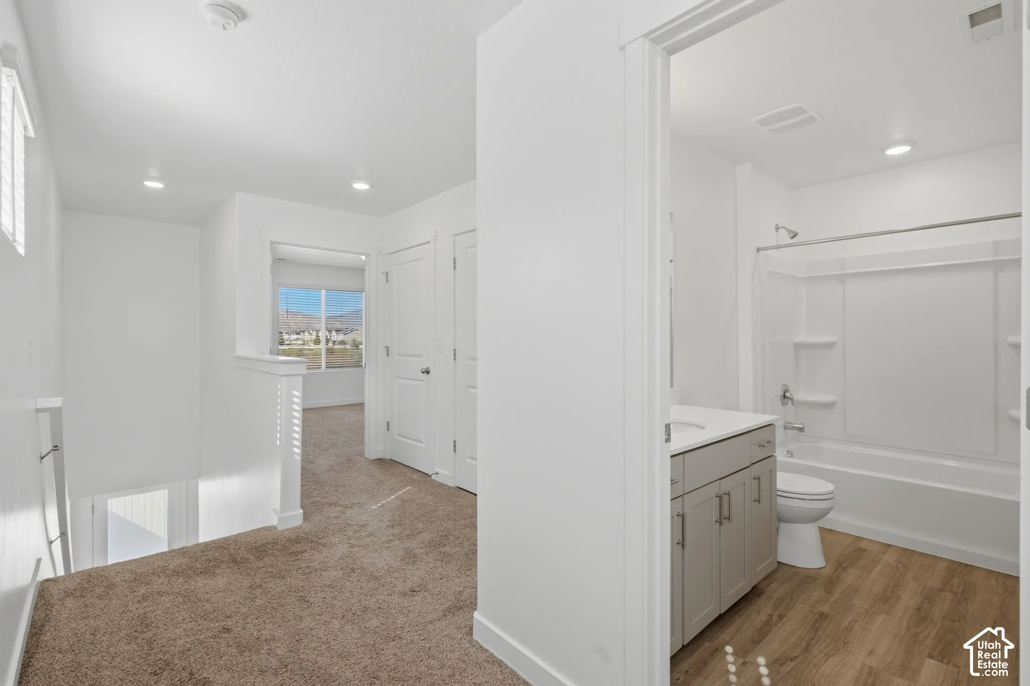 Recessed lighting, wood-finish flooring, white solid-surface vanity, and a shower/tub combination