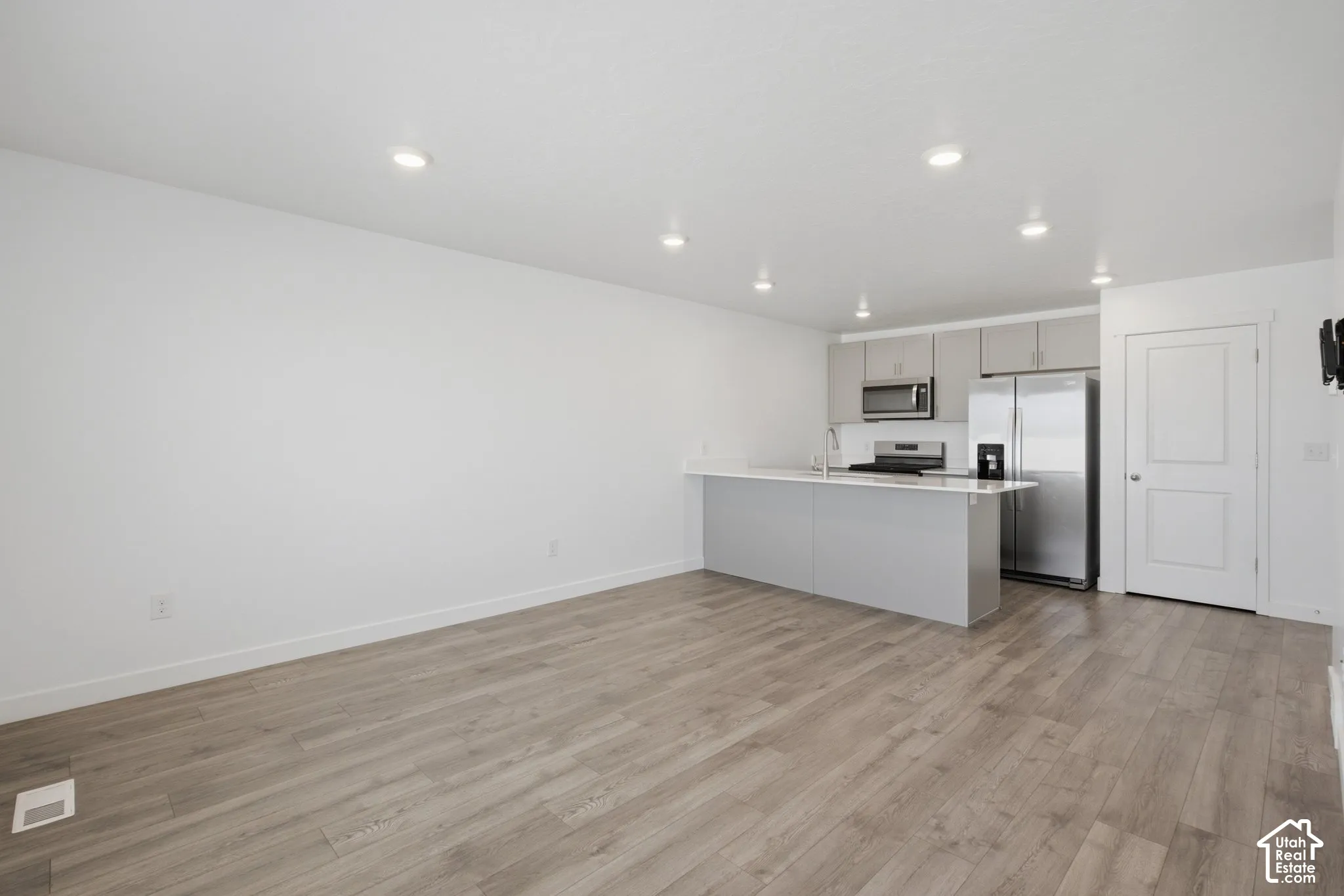 Open-concept living area featuring wood-finish flooring, recessed lighting, and a kitchen with gray cabinetry, white countertops, and stainless steel appliances