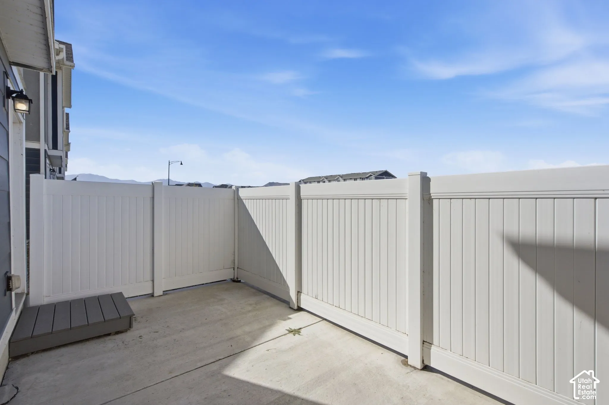 Concrete patio with a composite step, white vinyl fencing, and an exterior wall light