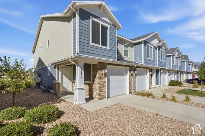 Townhome exterior with blue siding, stone facade, covered entry, and attached garage