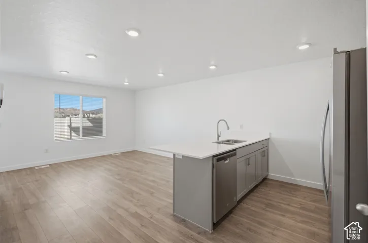 Open-concept living area featuring wood-finish flooring, recessed lighting, a kitchen island with an undermount sink and stainless-steel appliances, and a window with mountain scenery