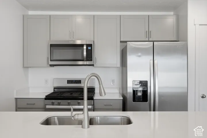 Kitchen featuring light gray cabinetry, stainless steel appliances, white countertops, and an undermount sink with a gooseneck faucet