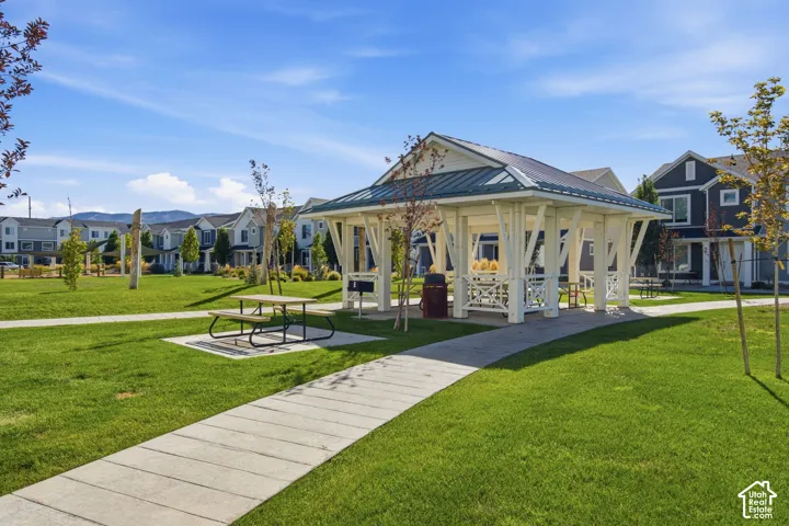 Expansive green space featuring a white gazebo with a dark roof, concrete pathways, and a picnic table