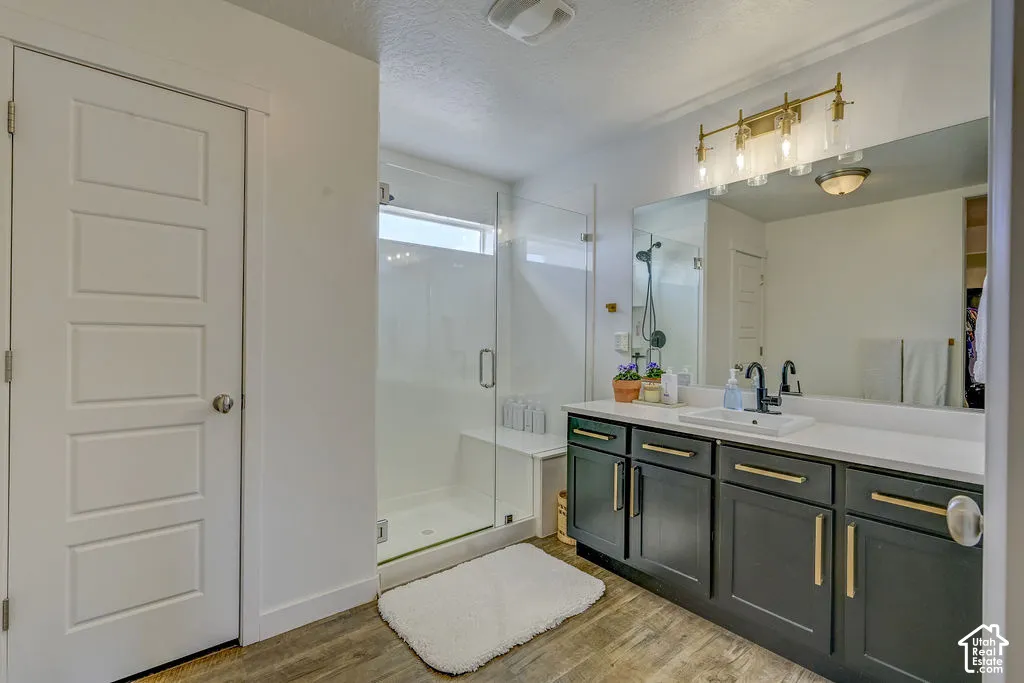 Spacious vanity with a white countertop and dark cabinetry, large walk-in shower with a built-in bench, and wood-finish flooring