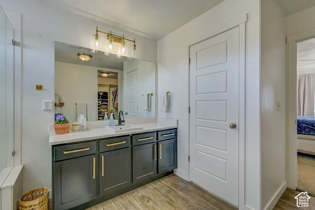Vanity featuring a white countertop, undermount sink with a black faucet, dark cabinetry with gold-tone hardware, and wood-finish flooring