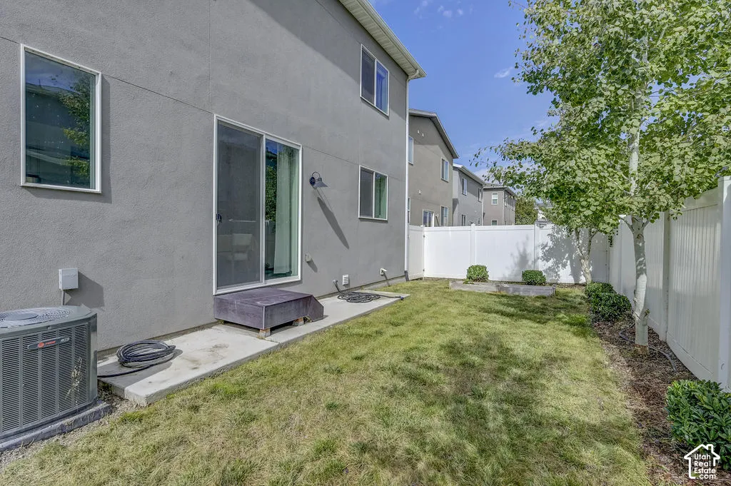 Private backyard with a sliding glass door, concrete patio, white vinyl fencing, and mature trees