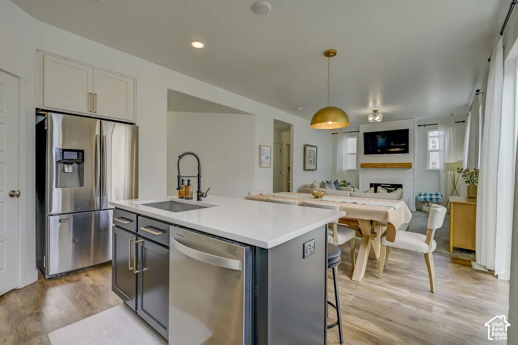 Kitchen island with a built-in sink, stainless steel appliances, wood-finish flooring, and a gold pendant light