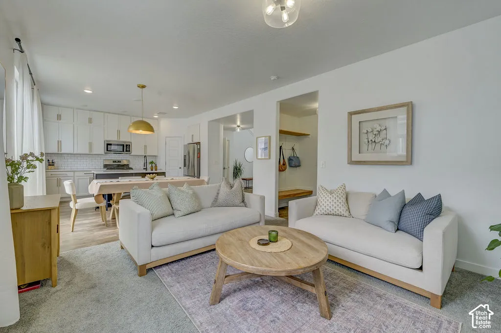 Open-concept living area featuring a kitchen with white cabinetry and stainless steel appliances, a dining area with a brass pendant light, and hard-surface flooring