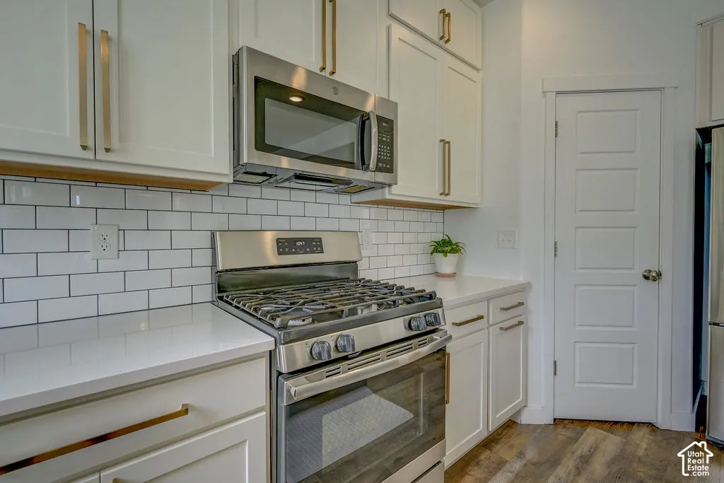 White shaker cabinetry with gold-tone hardware, stainless steel gas range, coordinating microwave, white subway tile backsplash, and wood-finish flooring