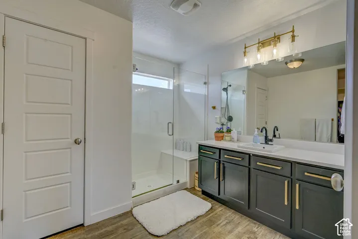 Spacious vanity with a white countertop and dark cabinetry, large walk-in shower with a built-in bench, and wood-finish flooring