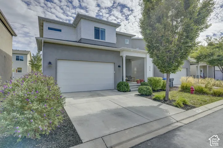 Stucco and siding exterior, attached garage, covered porch entry, mature landscaping, and concrete driveway