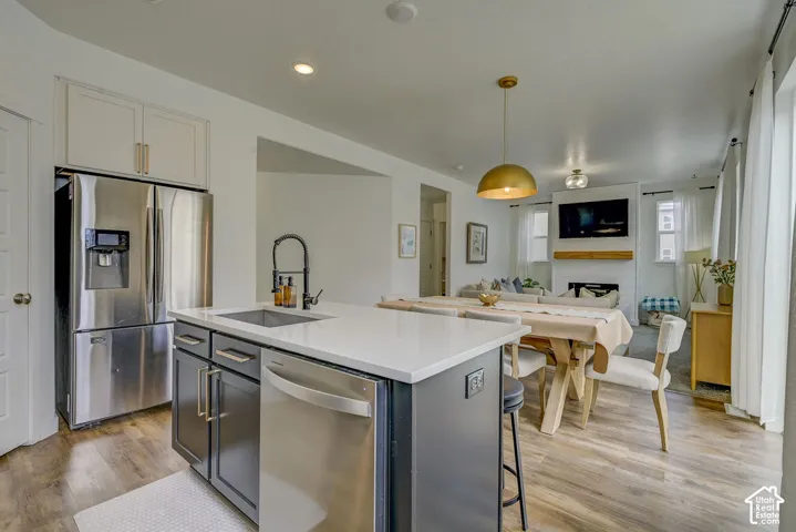 Kitchen island with a built-in sink, stainless steel appliances, wood-finish flooring, and a gold pendant light