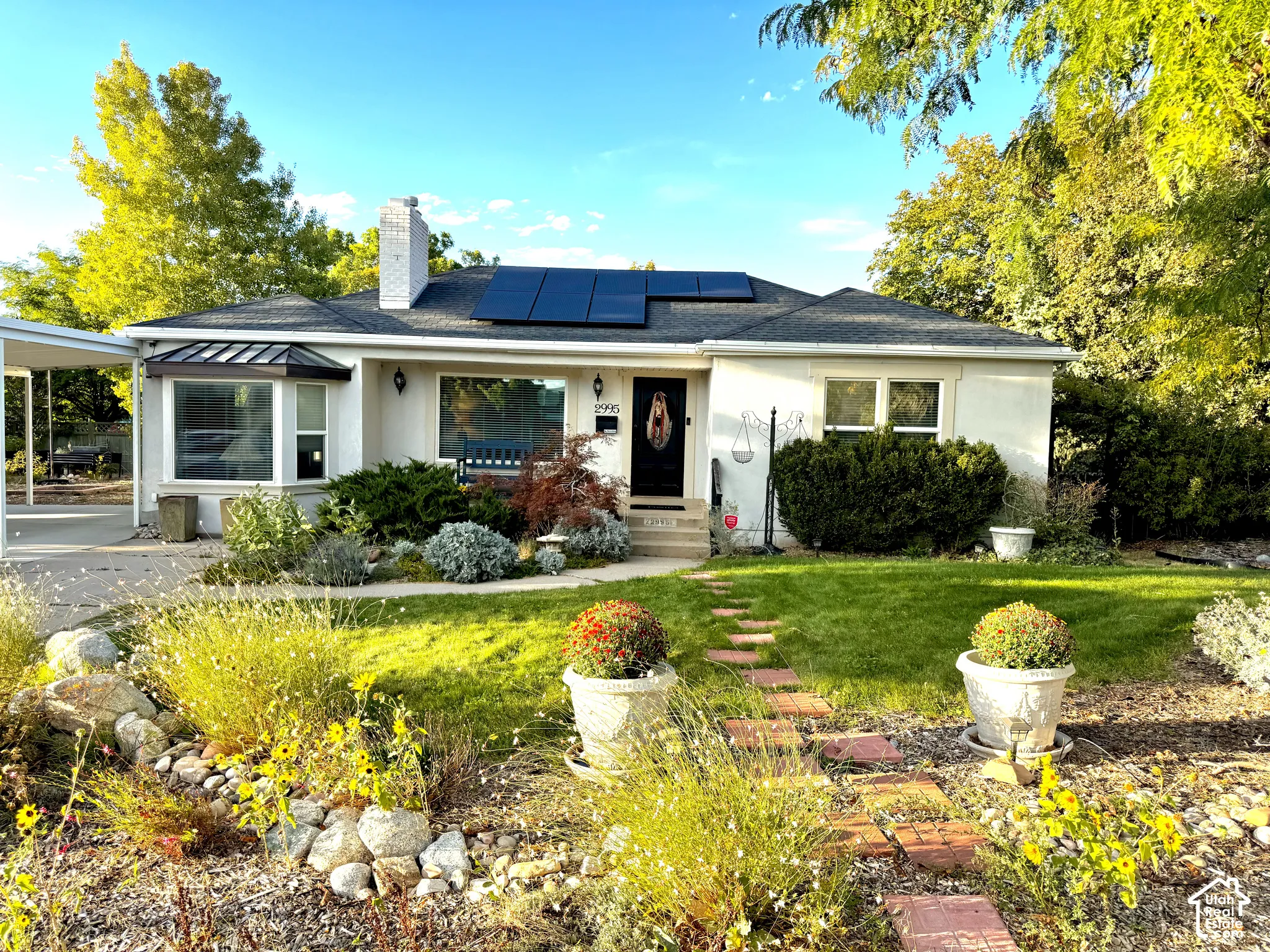 Stucco exterior with a bay window, carport, dark roof shingles, and solar panels