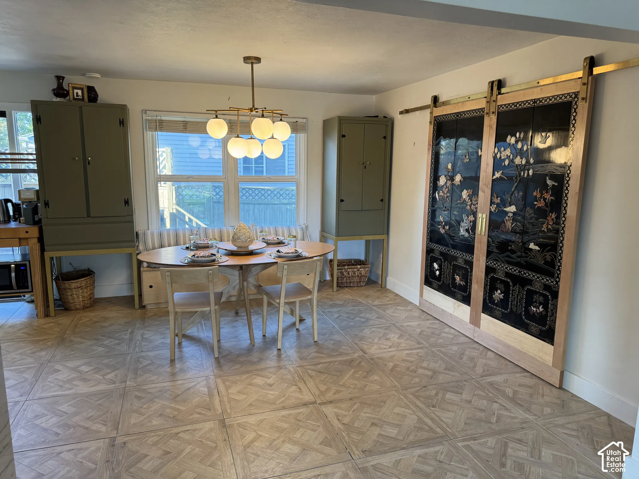 Parquet tile flooring, built-in window seating, decorative sliding barn doors, modern spherical chandelier, and multiple pane windows