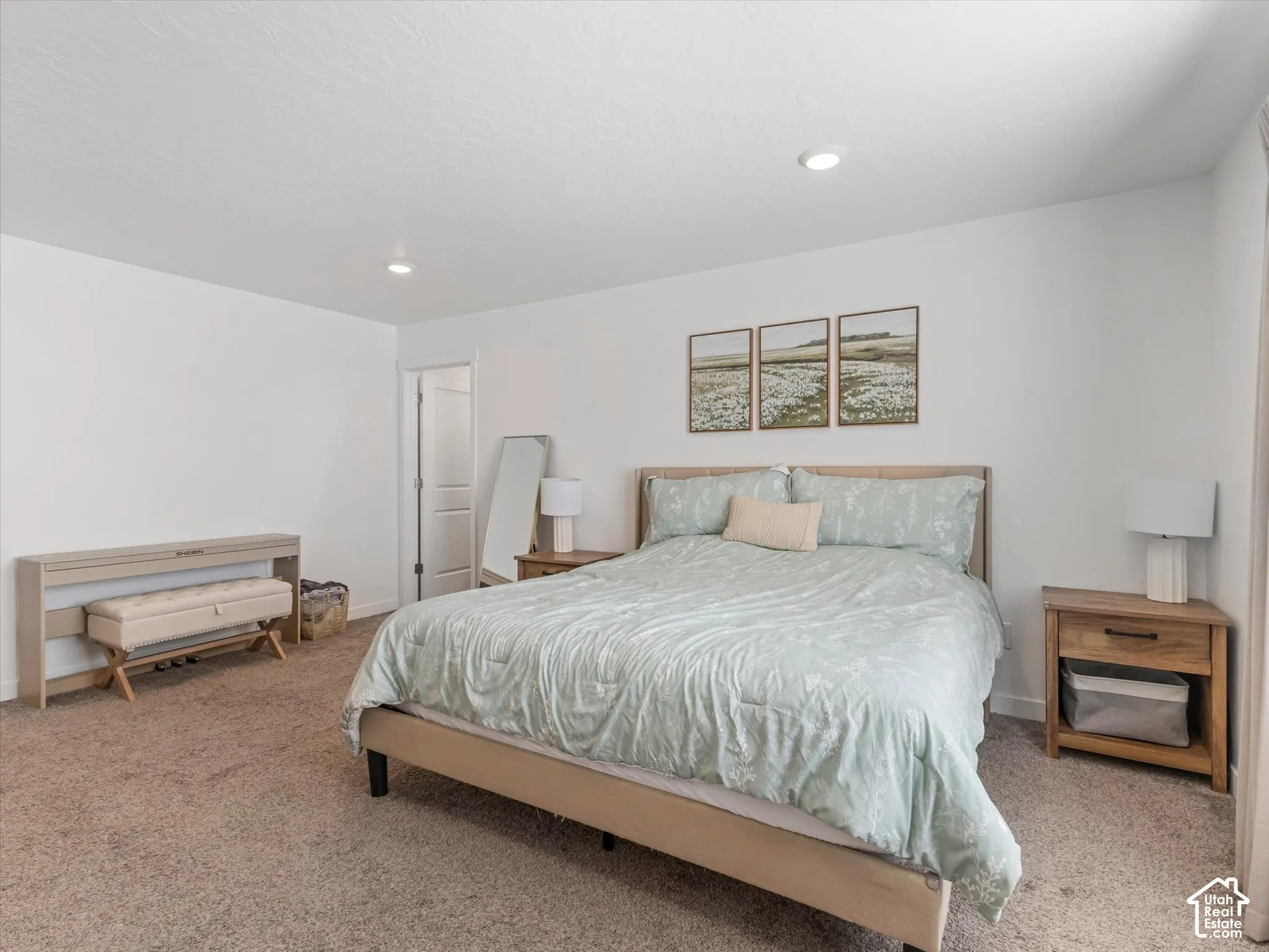Neutral tone carpeted flooring, recessed ceiling lighting, a solid panel interior door, and a wood-finish bed frame
