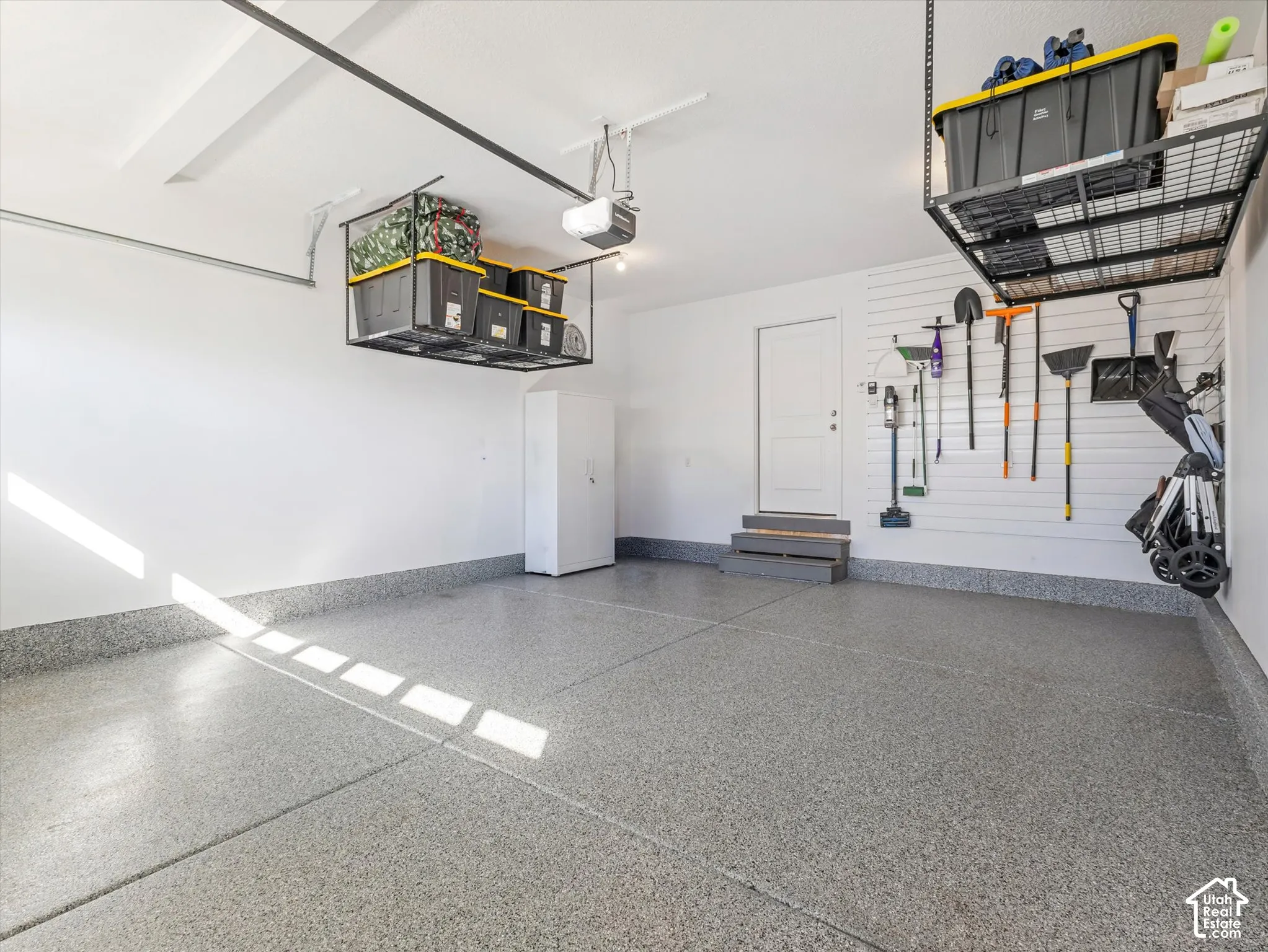 Coated concrete flooring, white walls, built-in overhead storage racks, integrated wall organization system, and a side-entry door