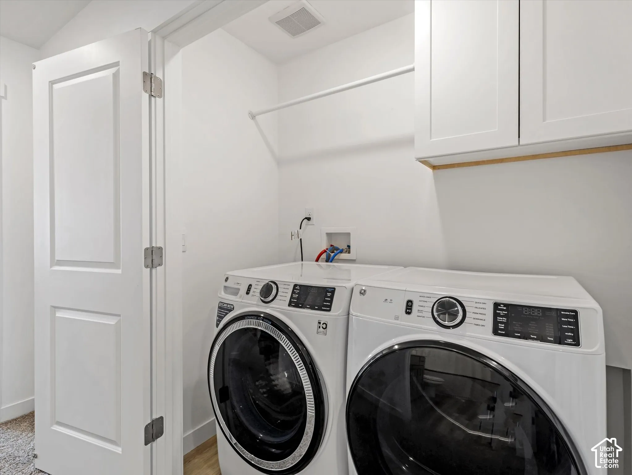 Recessed laundry area featuring white shaker-style cabinetry, a white hanging rod, and a white paneled door