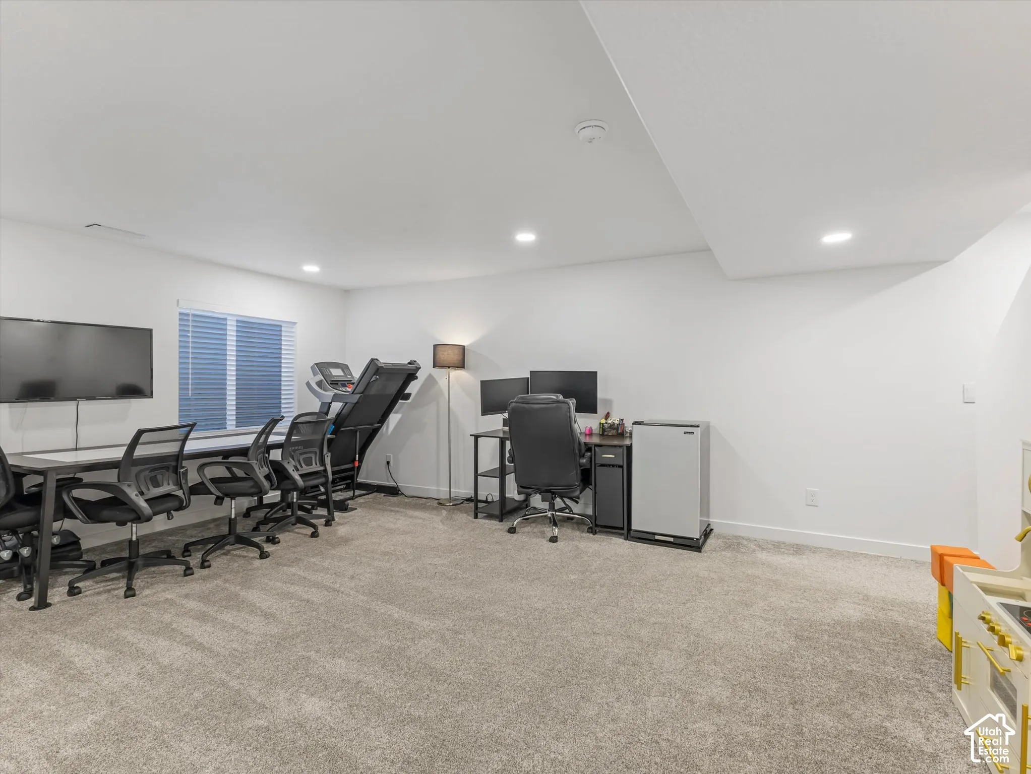 Spacious room featuring neutral carpeting, white walls, recessed lighting, and a window with blinds