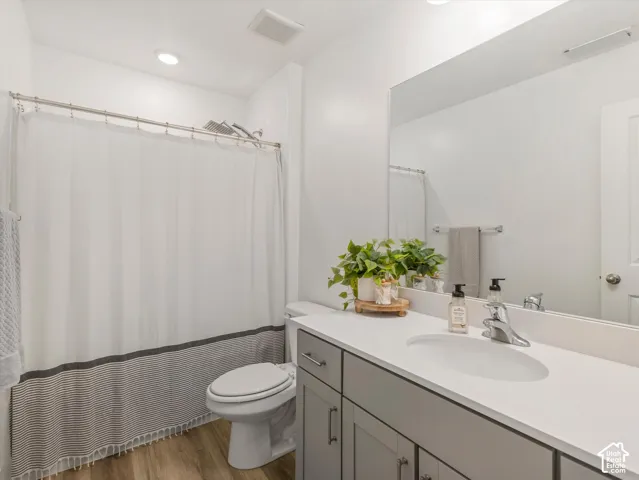 Bathroom featuring a vanity with a white countertop and undermount sink, built-in cabinetry, and wood-finish flooring