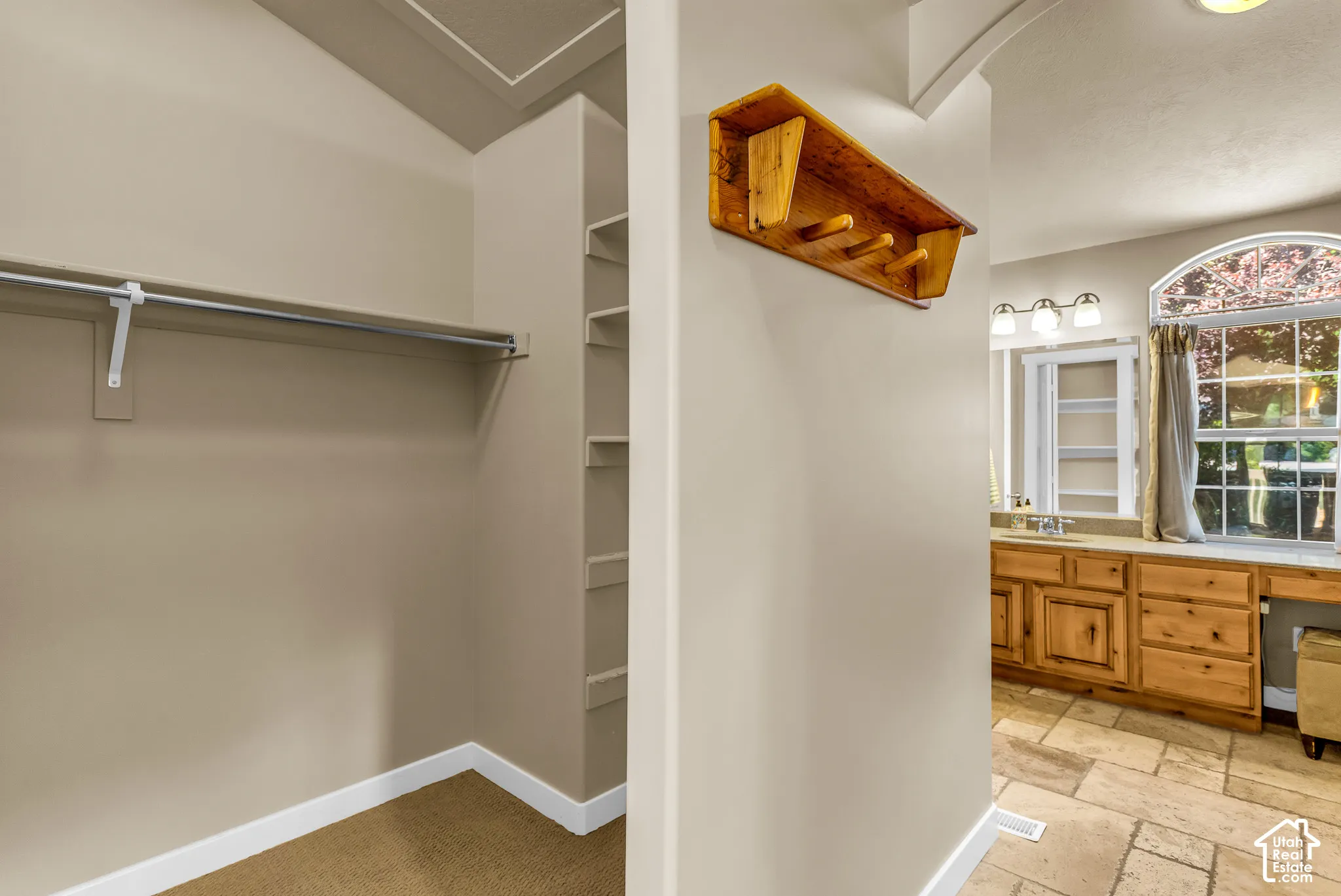 Built-in closet shelving, clothes hanging rod, arched window, wood cabinetry, and tile flooring