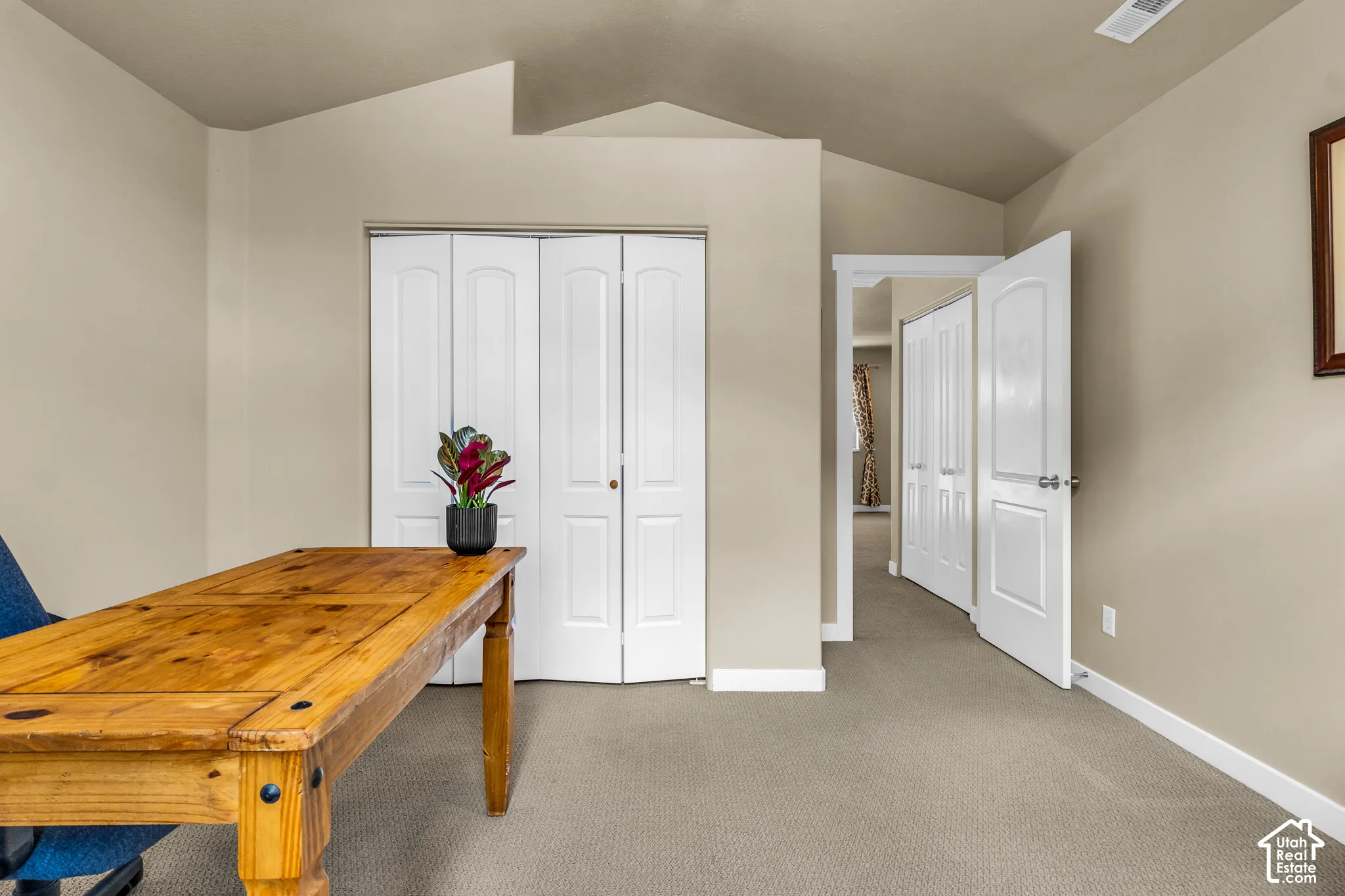 Vaulted ceiling with neutral wall tones, bi-fold closet doors, and carpet flooring