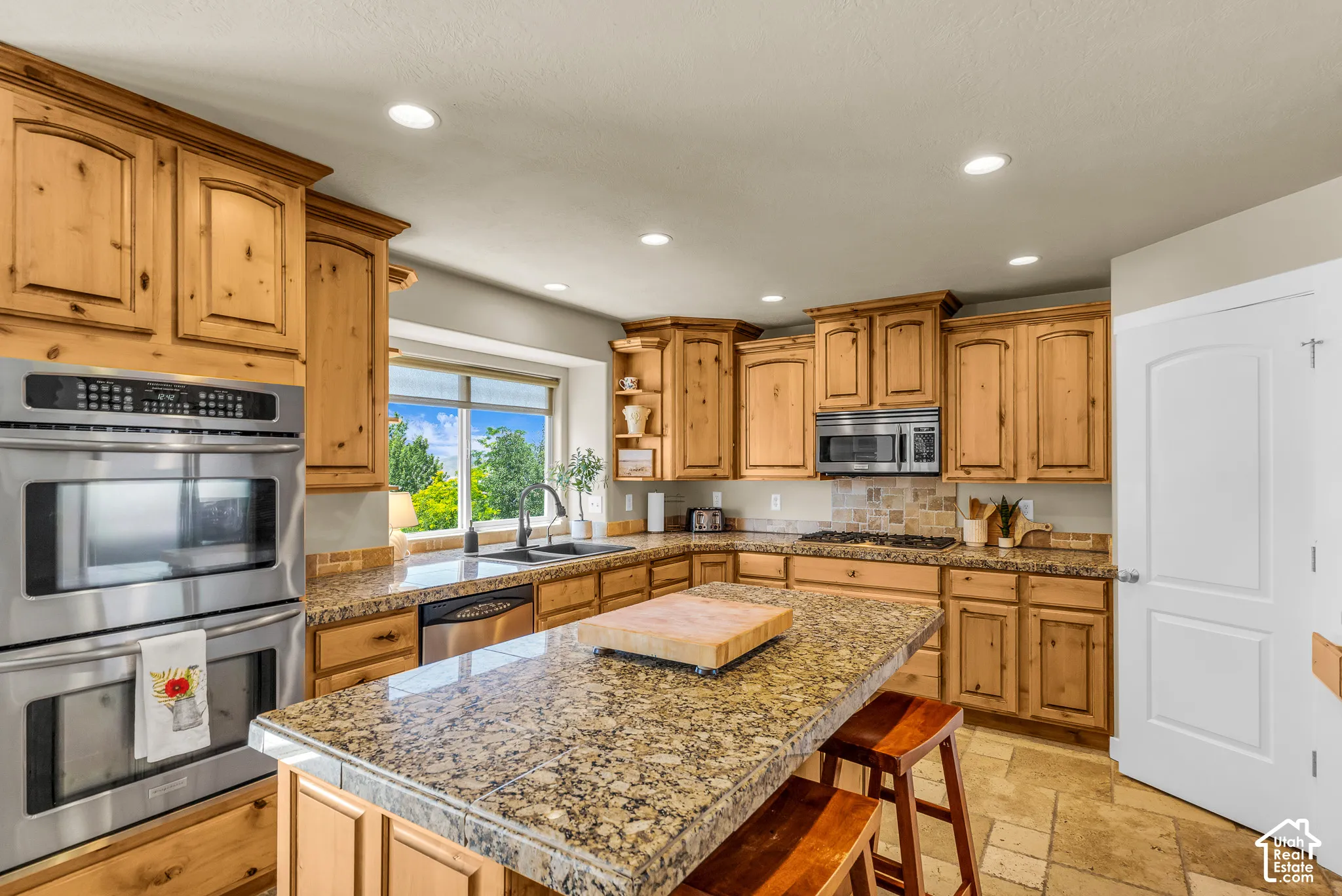 Wood-finish cabinetry, stainless steel double wall ovens, granite-style countertops, stainless steel microwave, and a tile backsplash