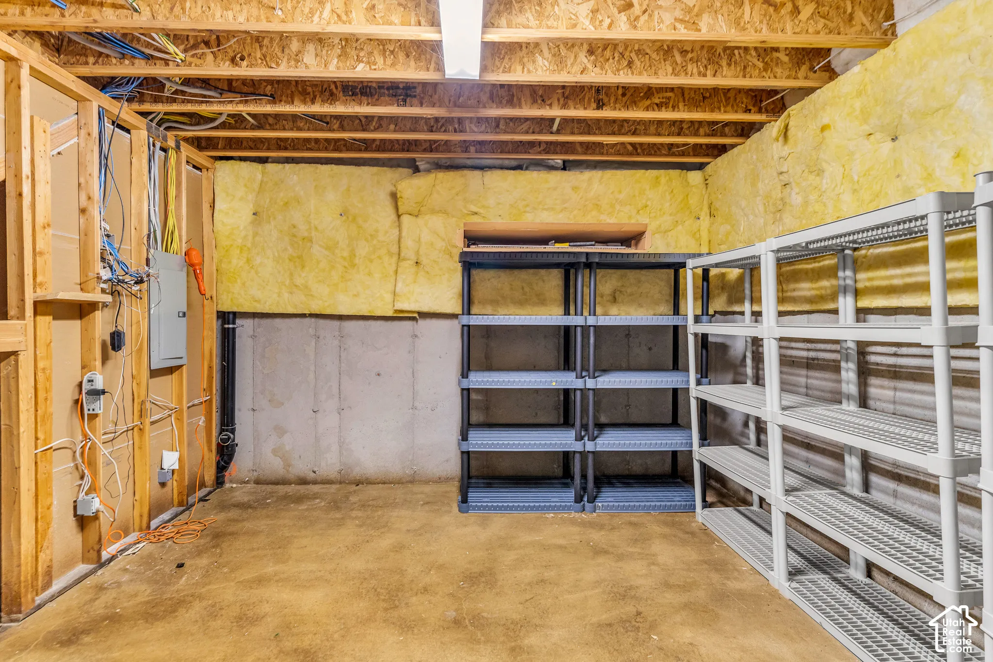 Unfinished basement space with exposed wooden joists, insulated walls, concrete flooring, and built-in shelving units