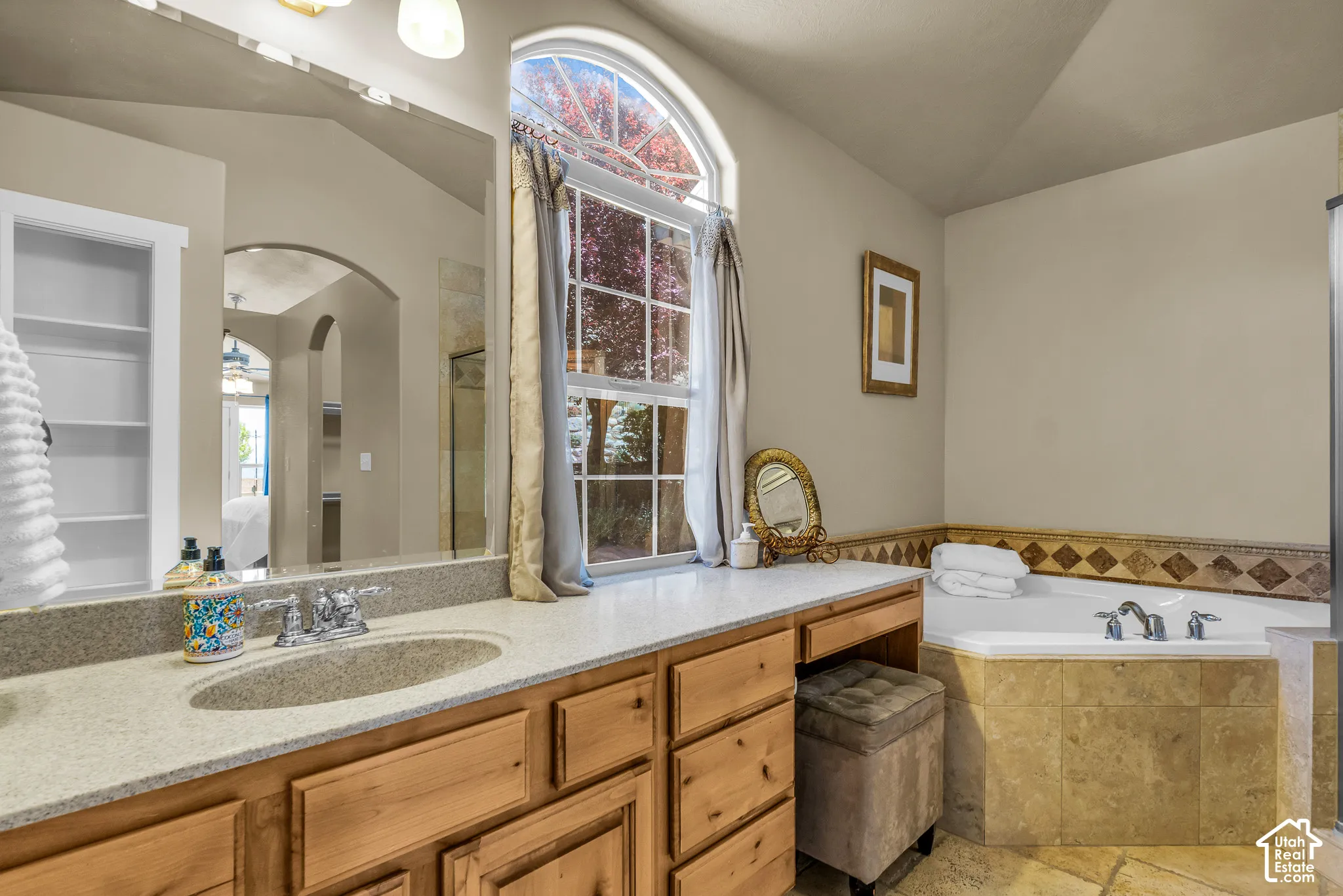 Built-in vanity with a single basin, arched window, built-in shelving, and a tiled soaking tub