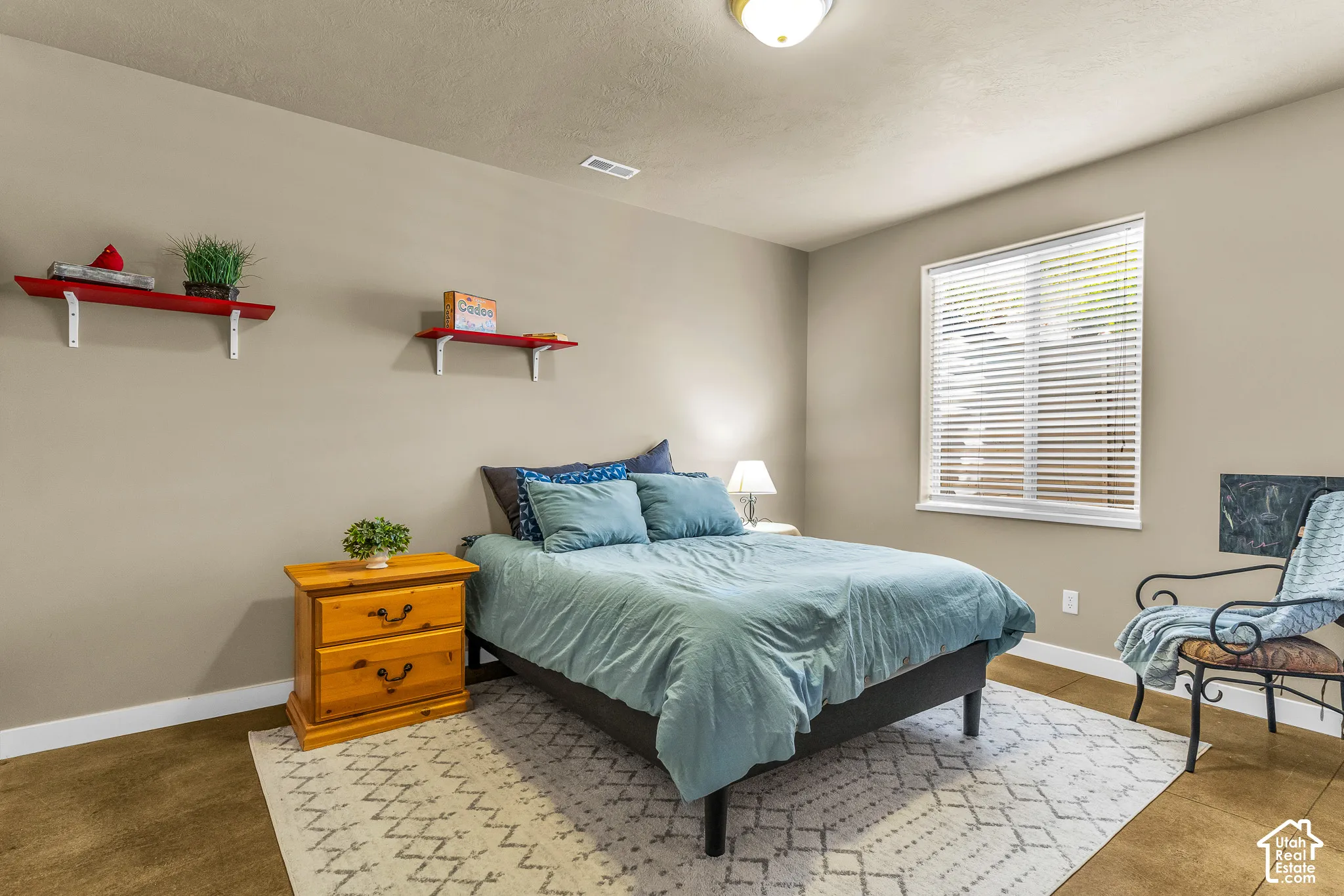 Wood-finish flooring with white trim, a single window with blinds, and two wall-mounted shelves