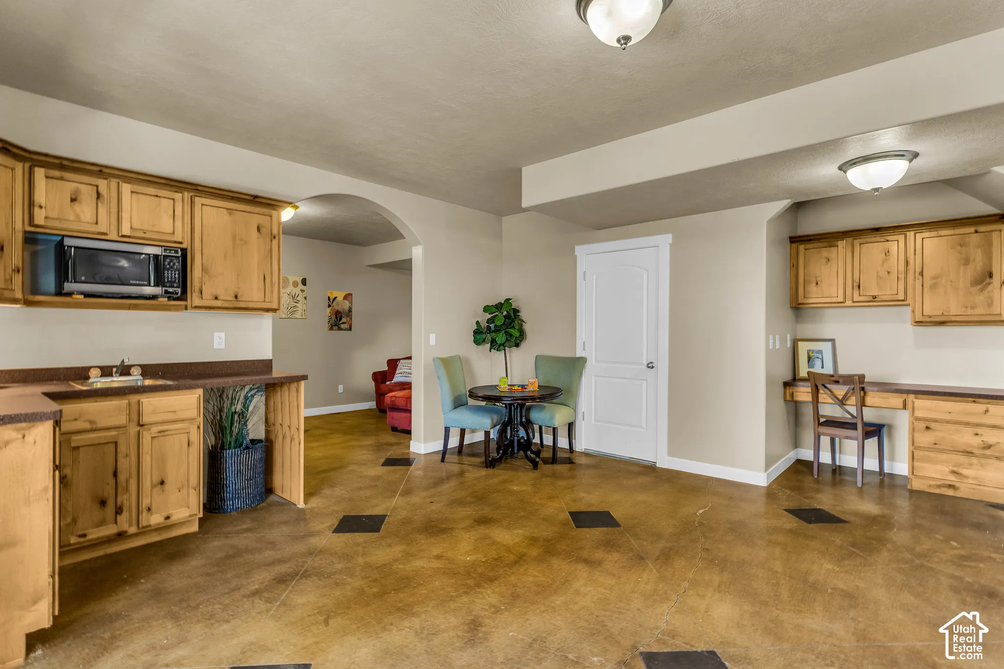 Stained concrete flooring, built-in desk, wood cabinetry, arched doorway, and a built-in wet bar