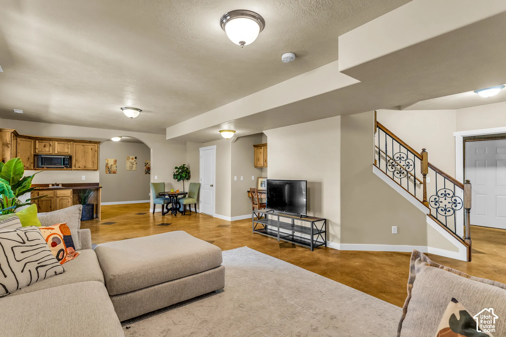 Hardwood-style flooring, wood cabinetry with built-in microwave, archway entry, and wrought iron staircase railing