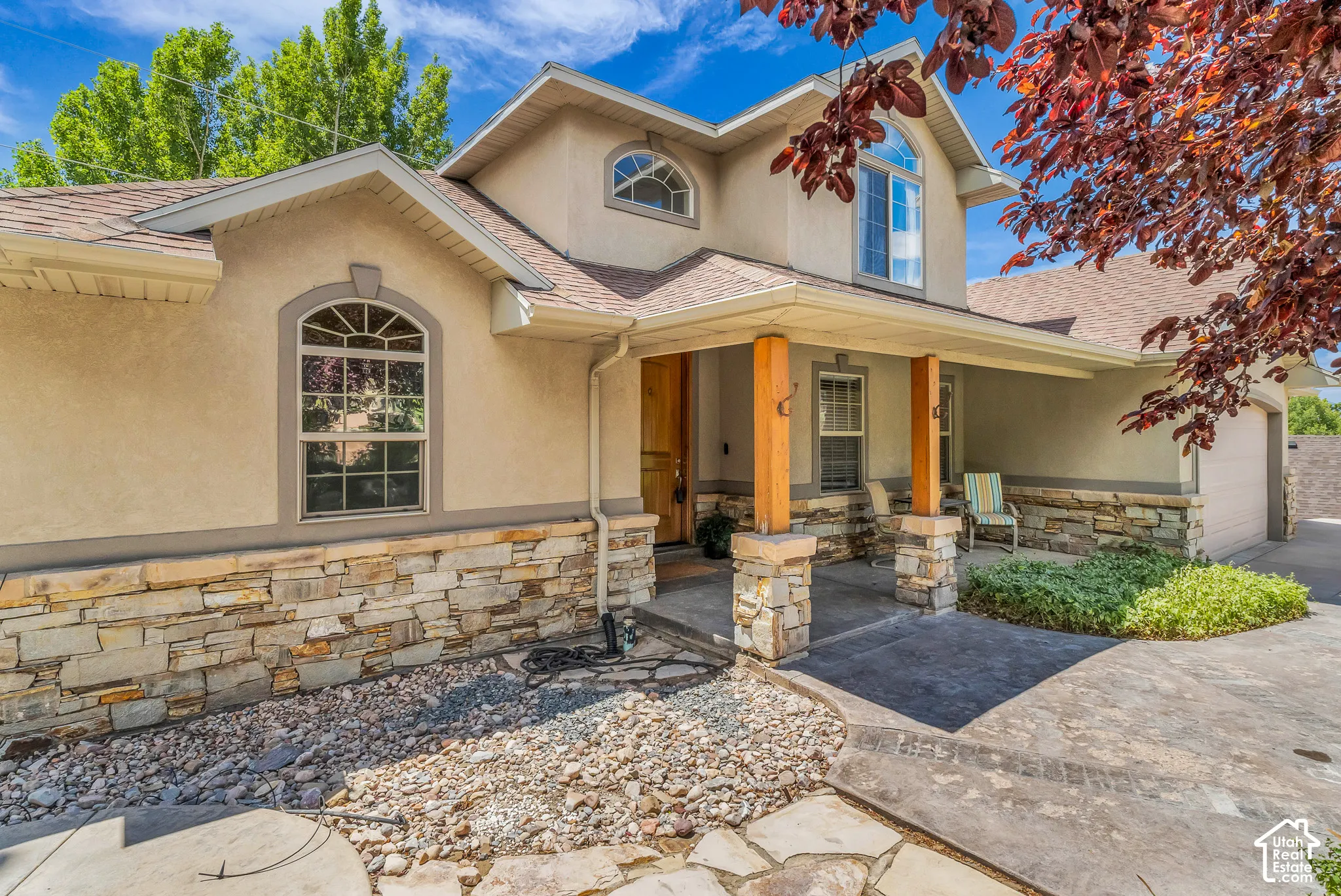 Stucco exterior with stone veneer accents, arched windows, covered porch with stone-wrapped columns and wood posts, and an attached garage