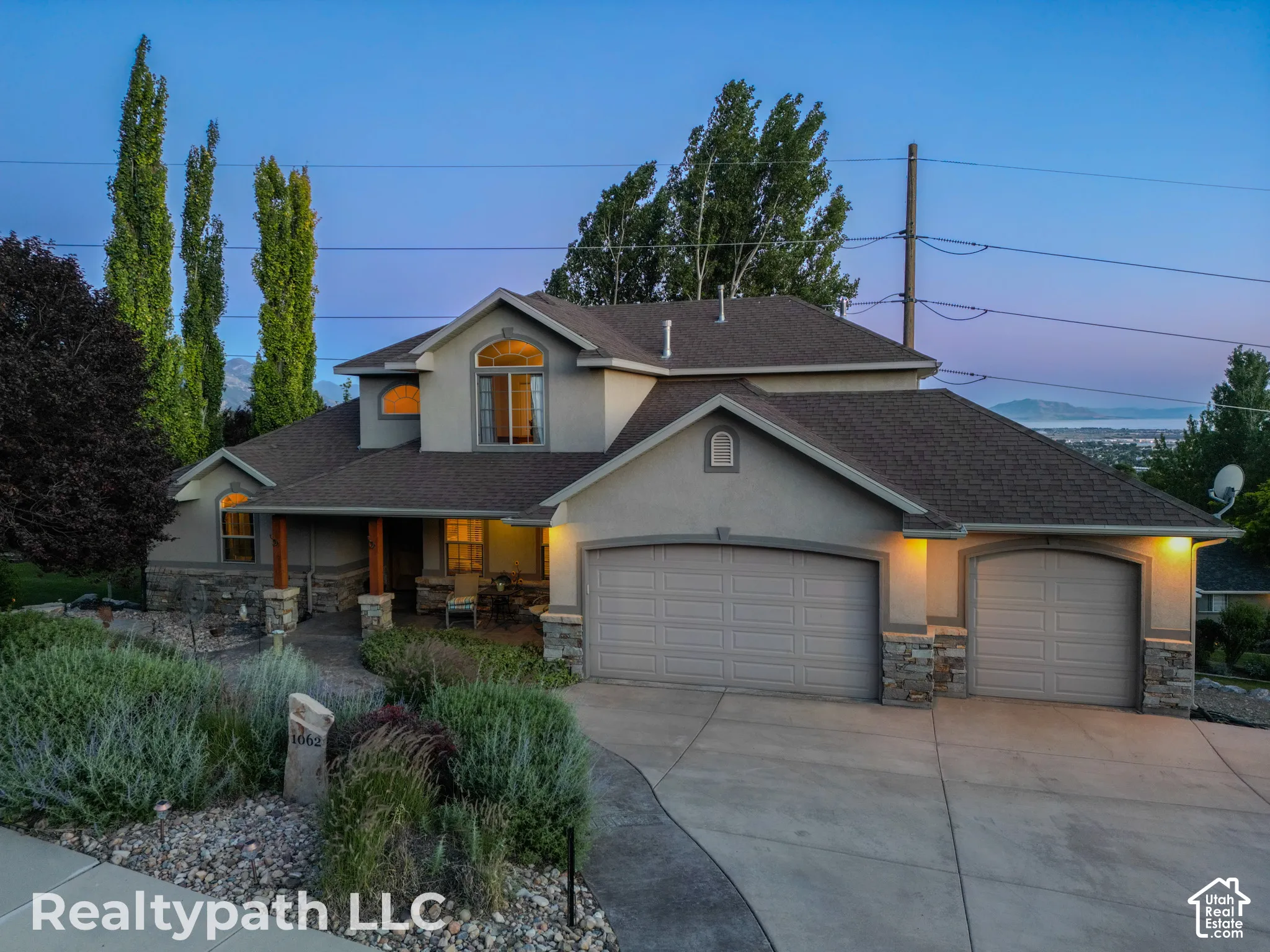 Stucco exterior with stone accents, covered front porch with wood columns, arched windows, attached double garage, and a concrete driveway