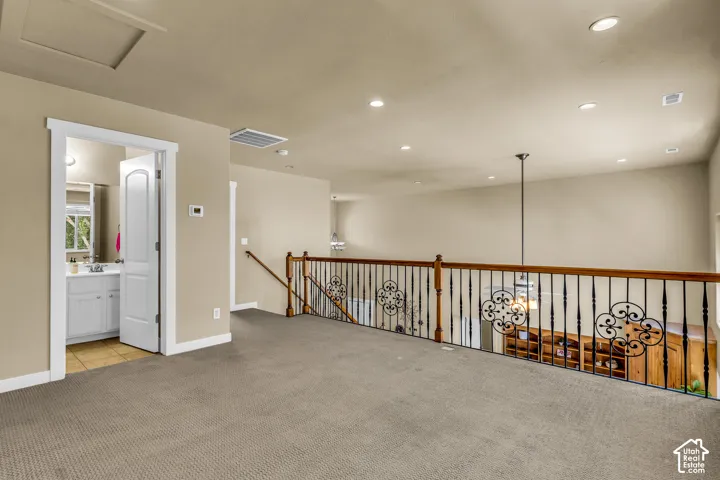 Carpeted interior with recessed lighting, an open doorway revealing a bathroom with a vanity and sink, and a staircase featuring wood railings with decorative iron balusters