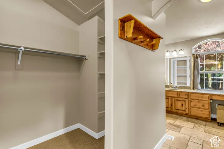 Built-in closet shelving, clothes hanging rod, arched window, wood cabinetry, and tile flooring