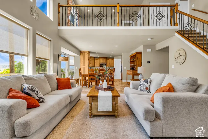 Two-story living area with high ceilings, large windows with roller shades, and a wood-finish staircase featuring decorative iron balusters